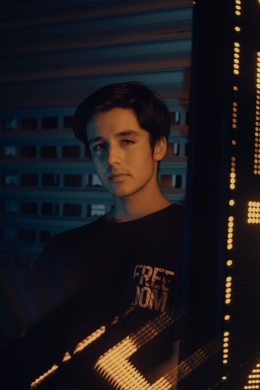 Junger Mann in dunklem Licht mit Neon-Reflexionen, nachdenklicher Ausdruck